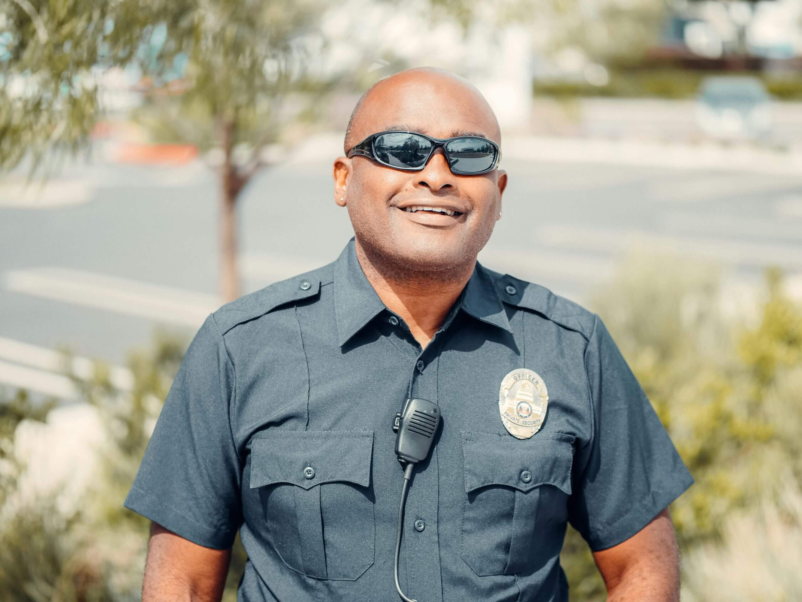 Portrait of a smiling police officer outdoors wearing sunglasses and uniform.