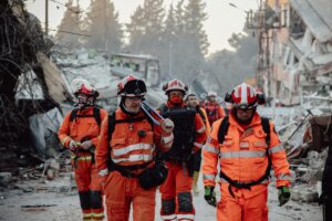 Search and rescue team in orange uniforms in a demolished area, assessing damage and carrying out operations.