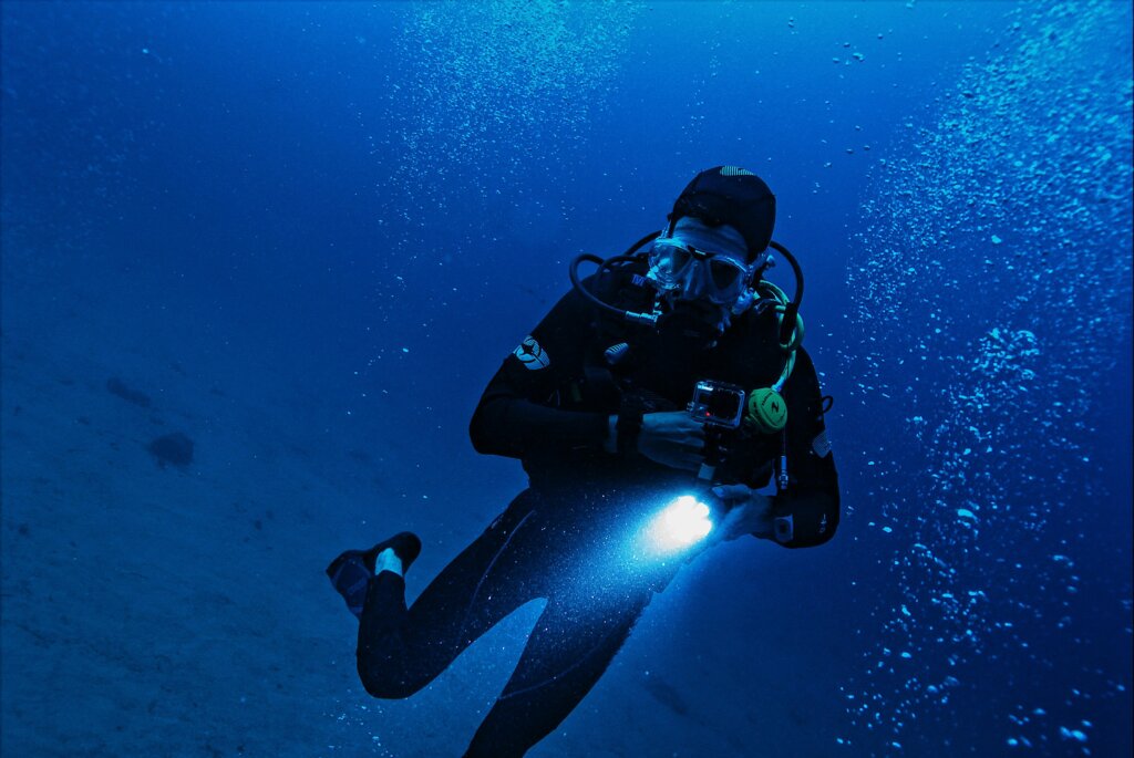 A scuba diver exploring the deep ocean with a flashlight, surrounded by bubbles and marine life.