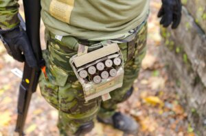 Close-up of a soldier in camouflage uniform with ammunition and shotgun outdoors.