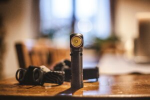 A vintage flashlight stands on a wooden table indoors, highlighting warm lighting.