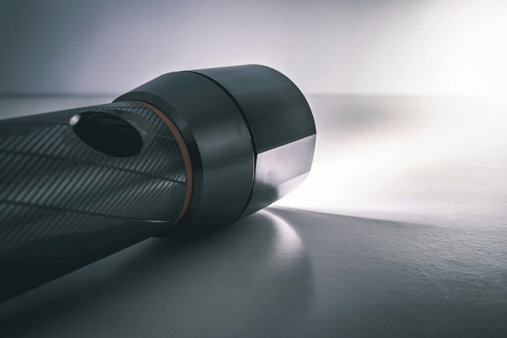 A close-up image of a metallic flashlight illuminated, highlighting its sleek design against a dark background.