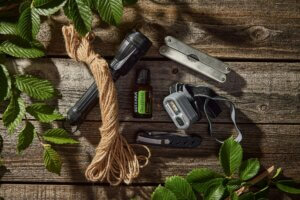 Collection of outdoor essentials including flashlights, rope, pocket knife, and essential oil on a wooden surface.