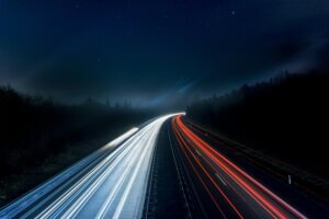 Long exposure night shot capturing stunning red and white light trails on a highway under a starry sky.